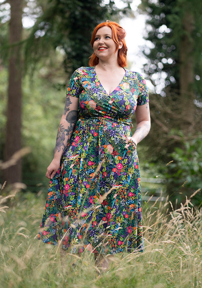 Woman in a colourful floral midi dress standing in a forest with hand in pocket
