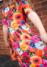 Colourful floral print dress worn by a child against a brick wall.