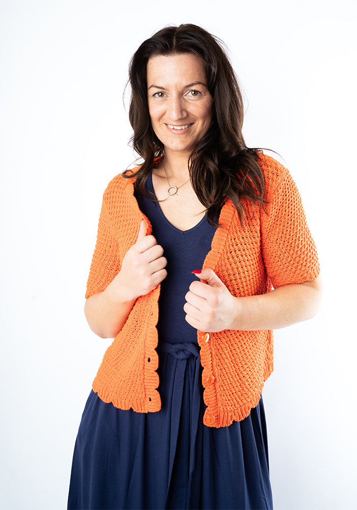 Woman wearing an orange knitted cardigan over a blue dress on a white background