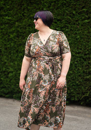 Woman wearing a floral dress standing against a green hedge.