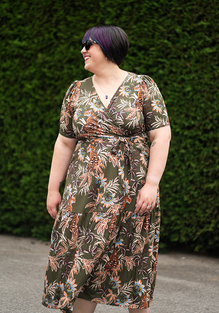 Woman wearing a floral dress standing against a green hedge.