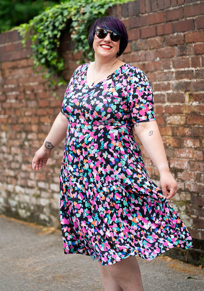 Woman wearing a colourful animal print dress standing against a brick wall.