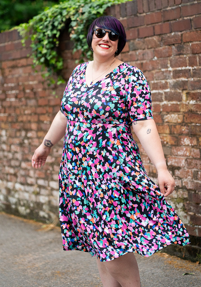 Woman wearing a colourful animal print dress standing against a brick wall.