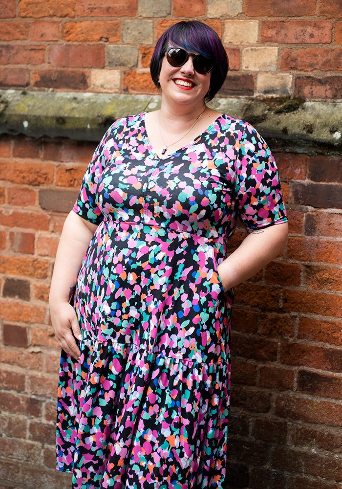 Woman wearing a colourful animal print dress and sunglasses against a brick wall with hand in pocket