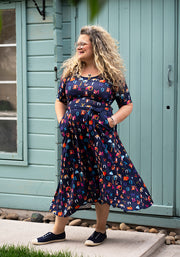Woman wearing a colourful letters phonics midi dress standing in front of a light blue building.