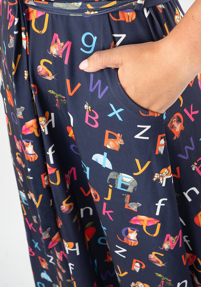 Navy blue midi dress with colourful alphabet phonics and animal pattern, with hand in pocket