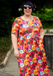 Person wearing a colourful floral and cat print dress outdoors with greenery in the background and hand in pocket