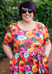 Person wearing a colorful floral dress with sunglasses against a green leafy background