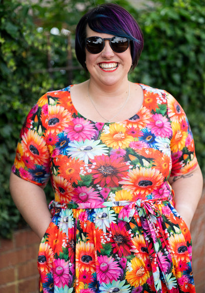 Person wearing a colorful floral dress with sunglasses against a green leafy background
