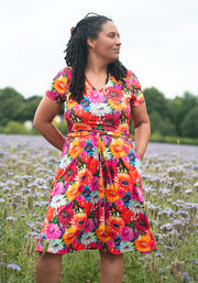 Woman wearing a colourful floral dress with hidden cats standing in a field with wildflowers.