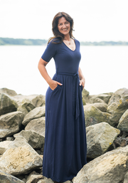 Woman in a navy blue maxi dress standing on rocks by a body of water