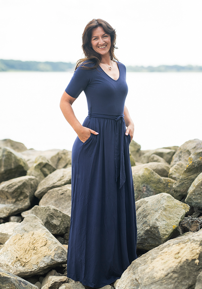 Woman in a navy blue maxi dress standing on rocks by a body of water