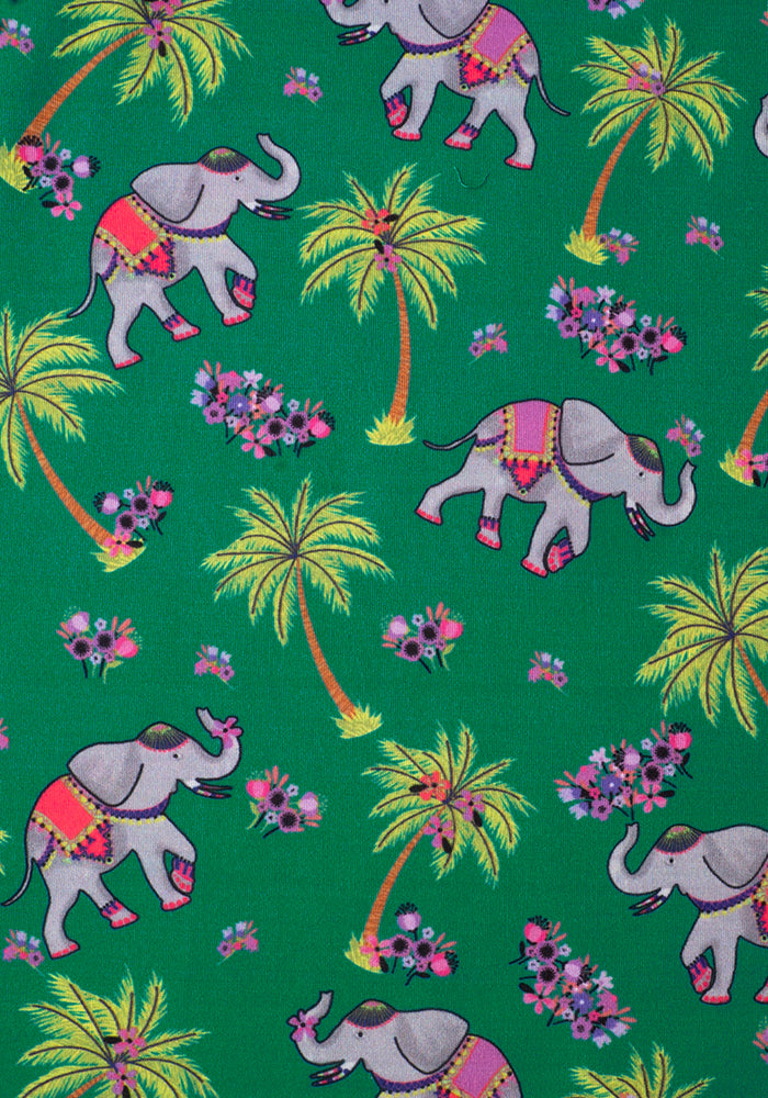 A close up of the print of Tantor. The dress has a green ground, with grey decorated elephants joyously dancing in and amongst palm trees and pink and purple flowers.  